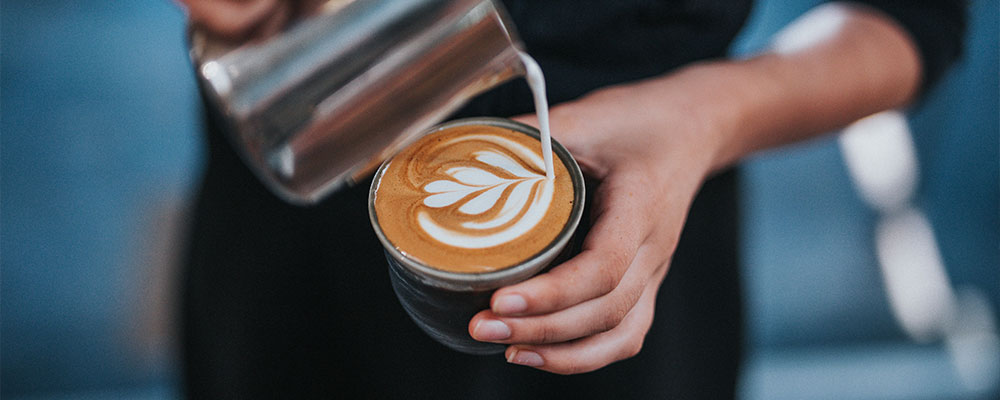 A barista pouring steamed milk into espresso