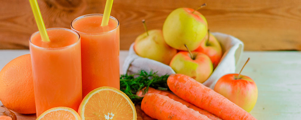 Two glasses of juice with carrots, oranges, and apples