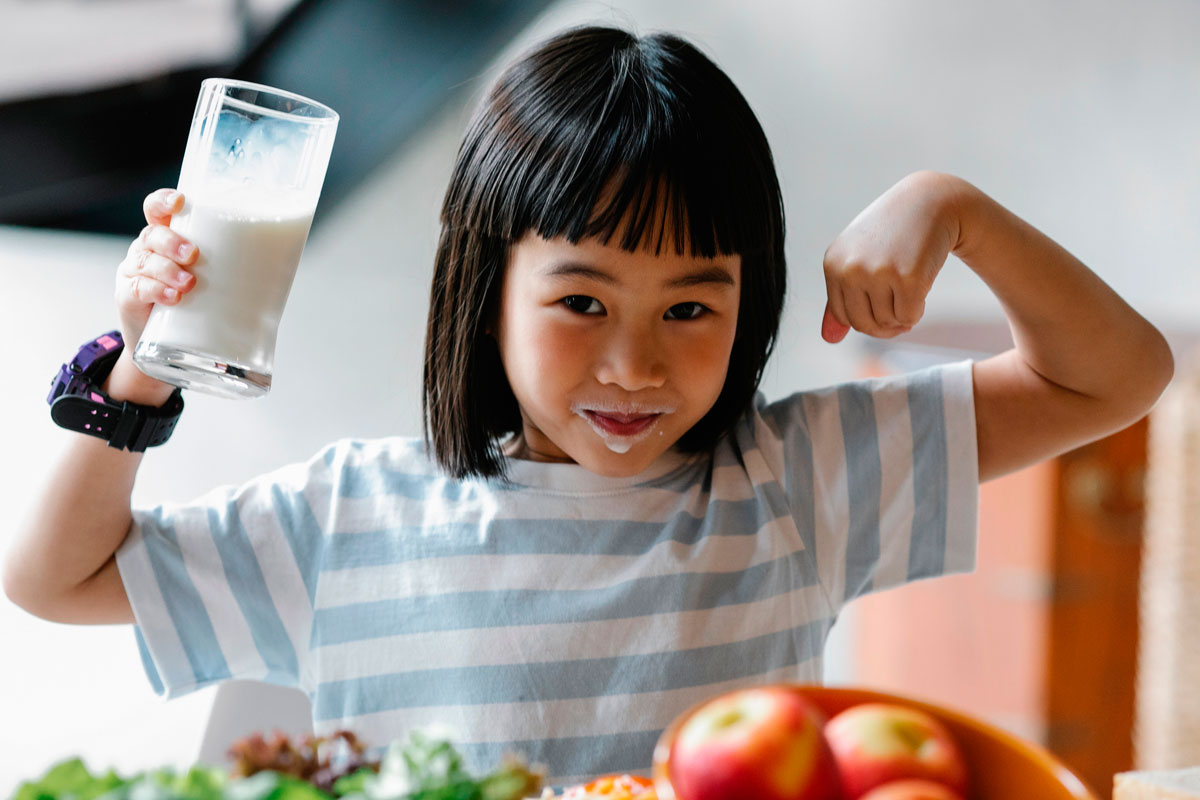 Young girl with a glass of milk flexing her muscles