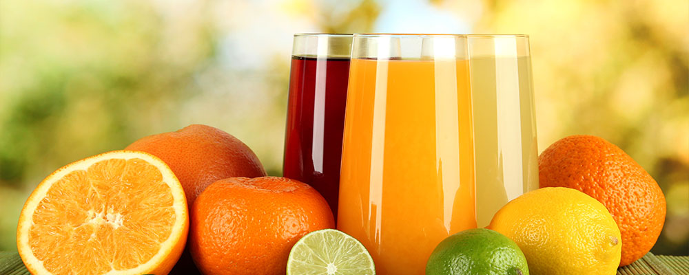A collection of fruits on a table with three glasses of juice